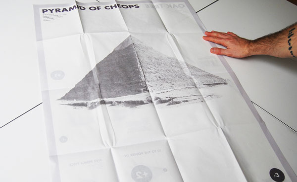 Two hands unravelling the booklet to sixteen times the size revealing a piece of content about a pyramid