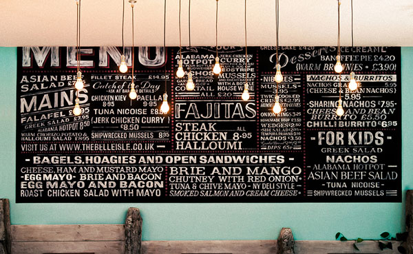 A chalkboard on a wall listing the food menu in various fonts and sizes