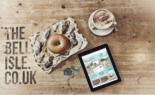 Top down view of table with bagel, coffee, keys and ipad with Belle Isle website
